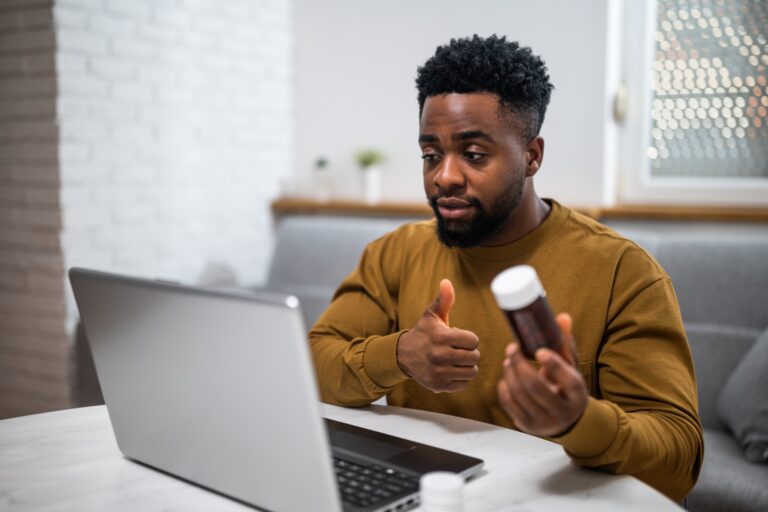 Young,Man,Showing,Pill,Bottle,To,Doctor,On,His,Laptop,